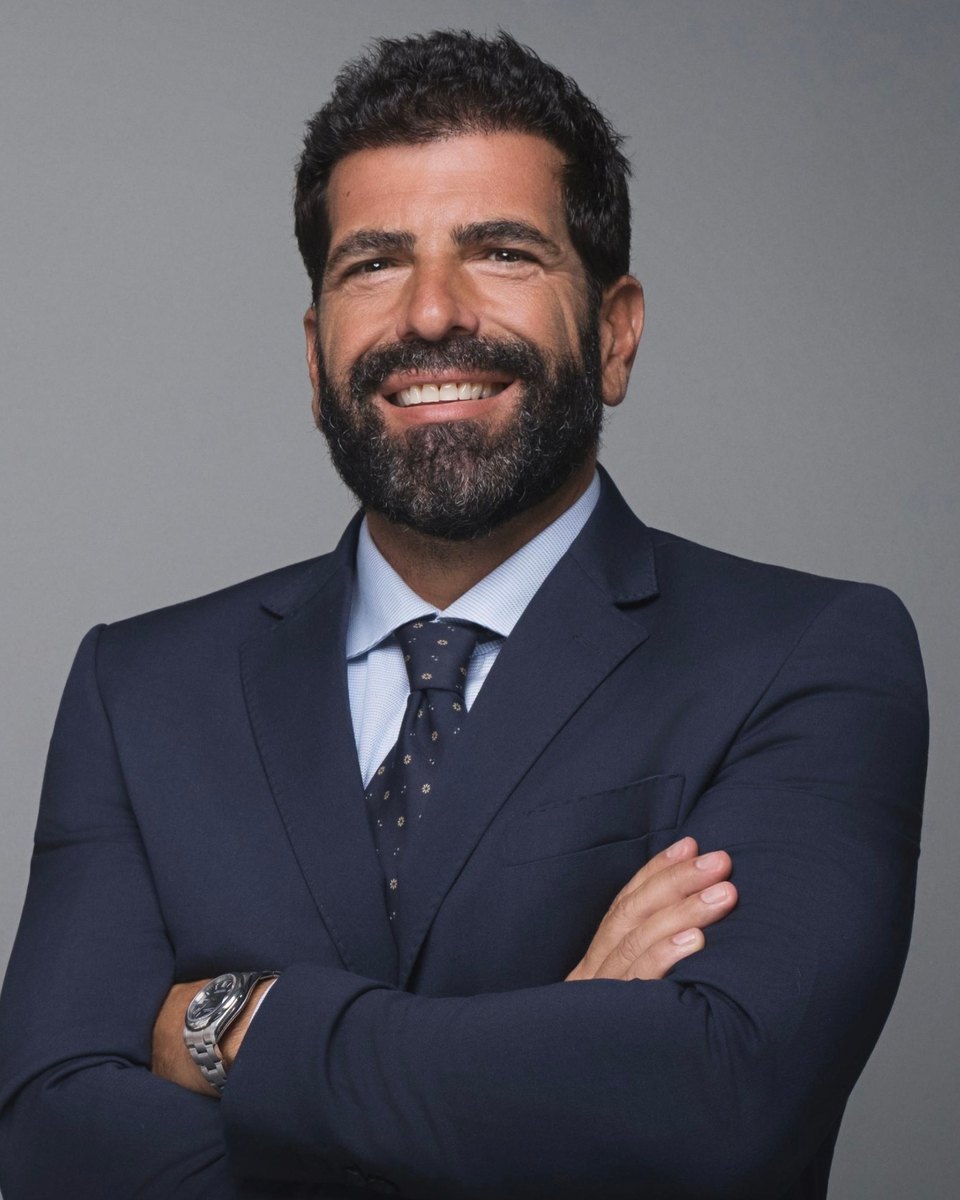 Portrait of Giovanni Gambardella smiling, arms crossed, in a navy suit